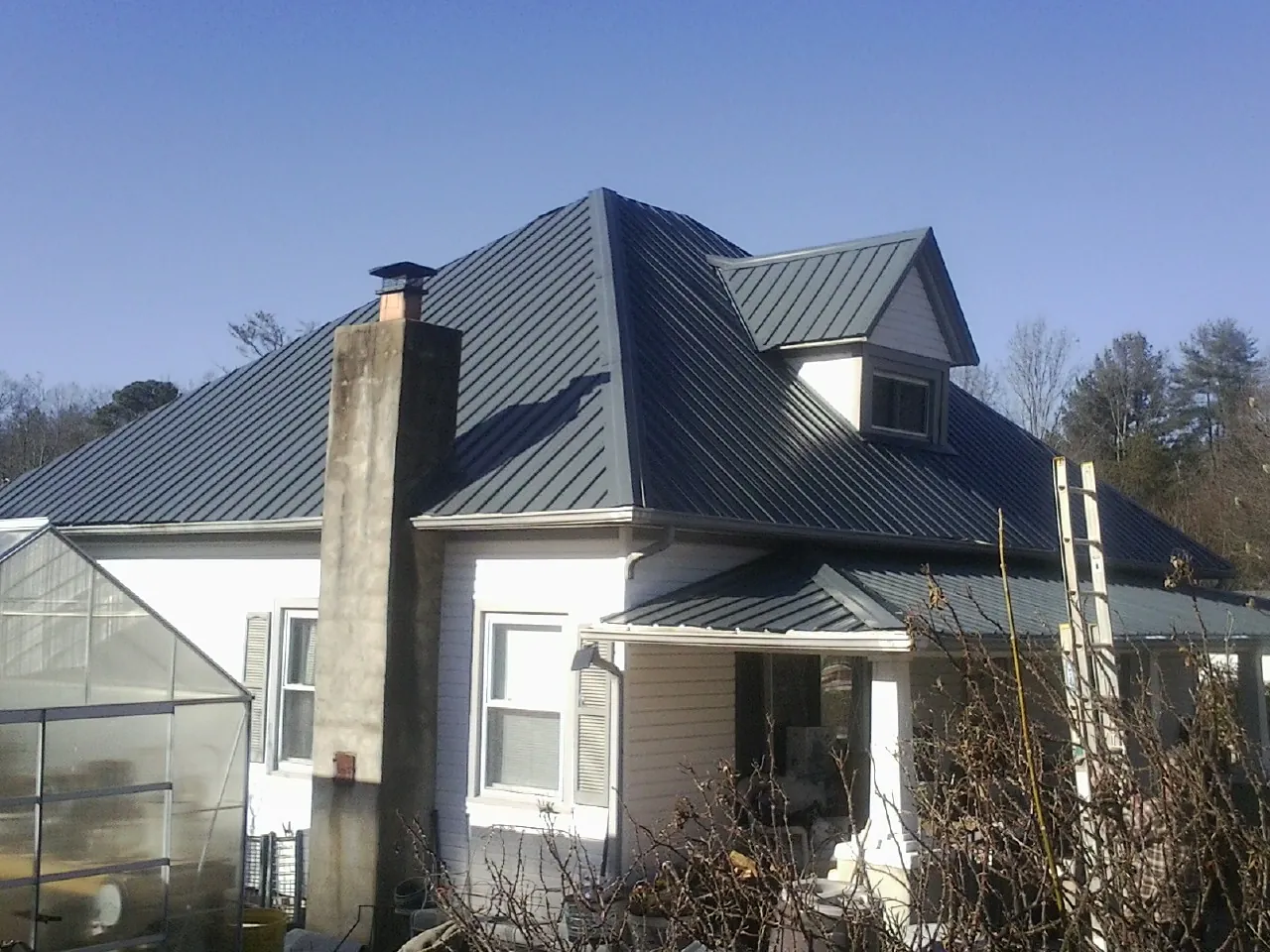 Dark blue standing seam metal roof on a white farmhouse with dormer — Slate & Tile Roof Repair by Roofing Brothers in Greenlawn