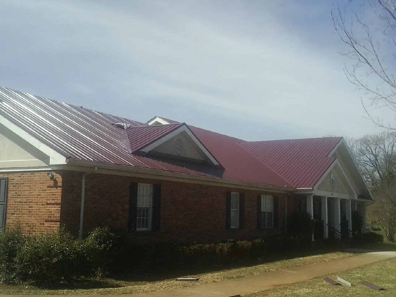Red metal roof with gabled entries on a long brick building, from a Hail Damage Roof Repair job in Greenlawn