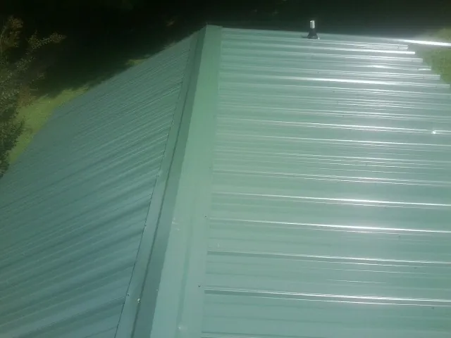 New green metal panels meeting at the ridge of a roof — Flat Roof Repair work by our crew in Greenlawn