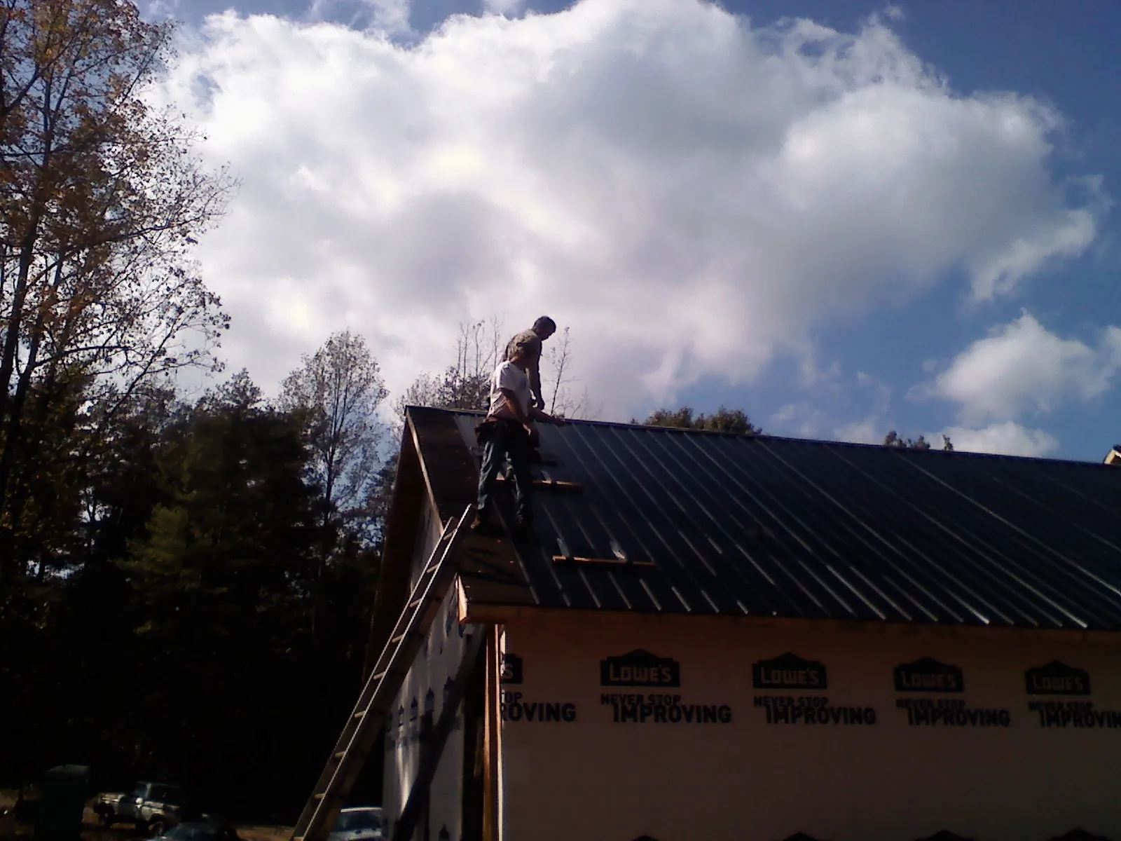 Roofer fastening dark metal panels high against a cloudy sky, from a Roof Inspection job in Greenlawn