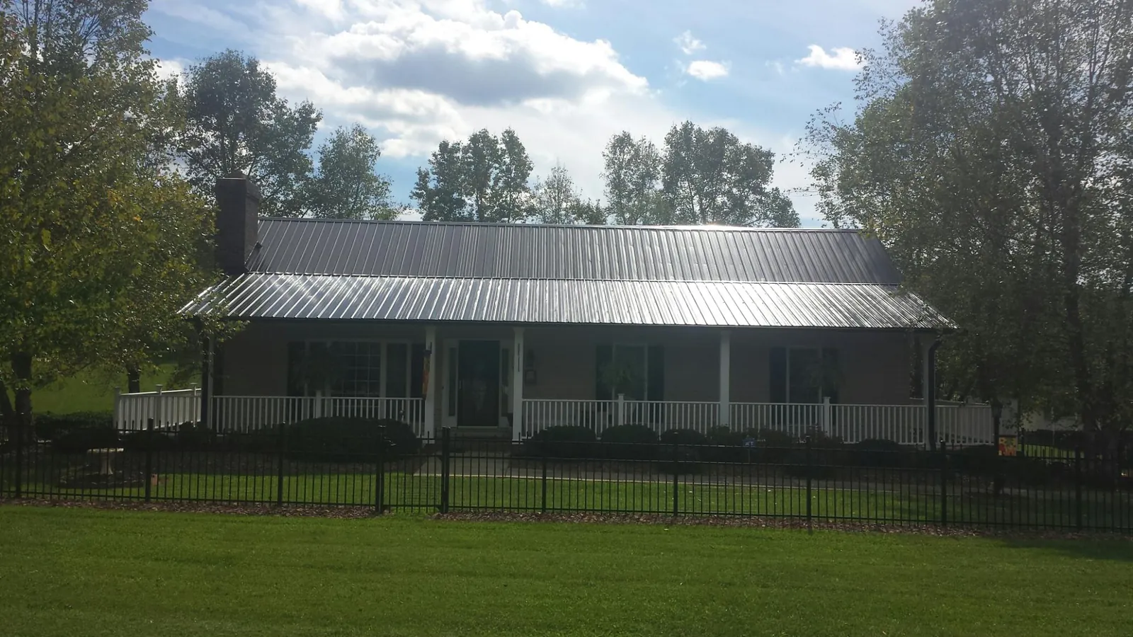 Gray metal roof on a brick ranch with a full width front porch — Gutter Guard Installation work by our crew in Greenlawn