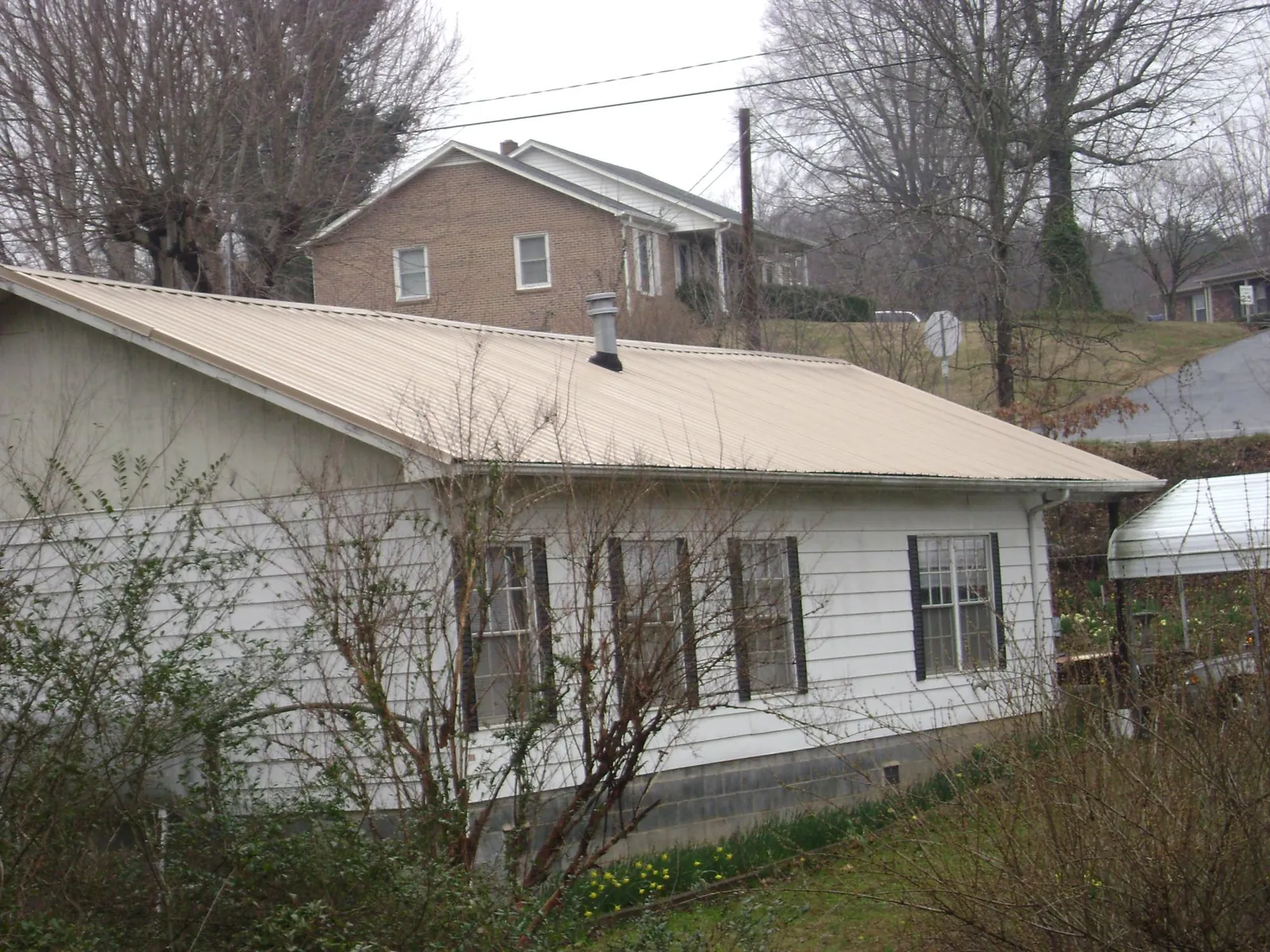Tan metal roof on a white sided house set into a hillside — Commercial Roofing by Roofing Brothers in Greenlawn
