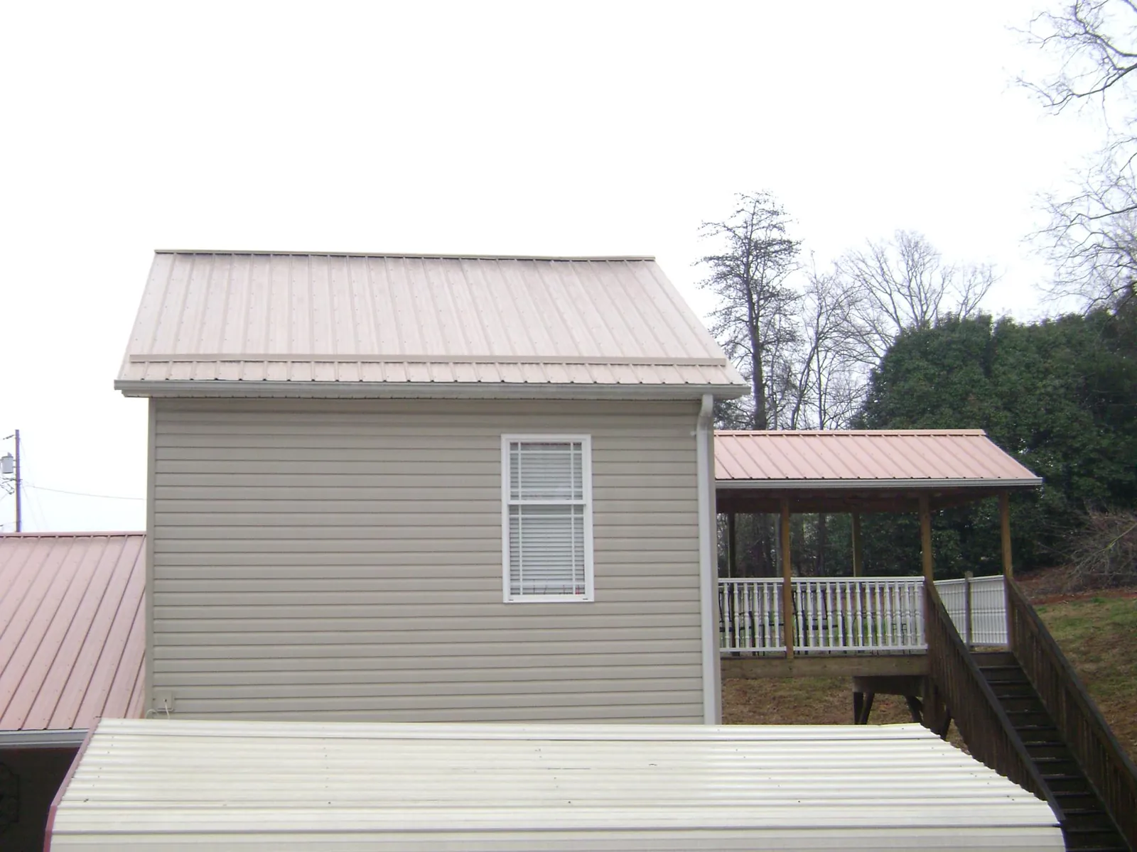 Tan metal roofs on a two story addition and attached porch, from a Roof Replacement job in Greenlawn